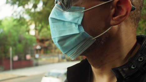 hombre parado afuera en un día soleado usando una máscara quirúrgica covid-19 y gafas de sol