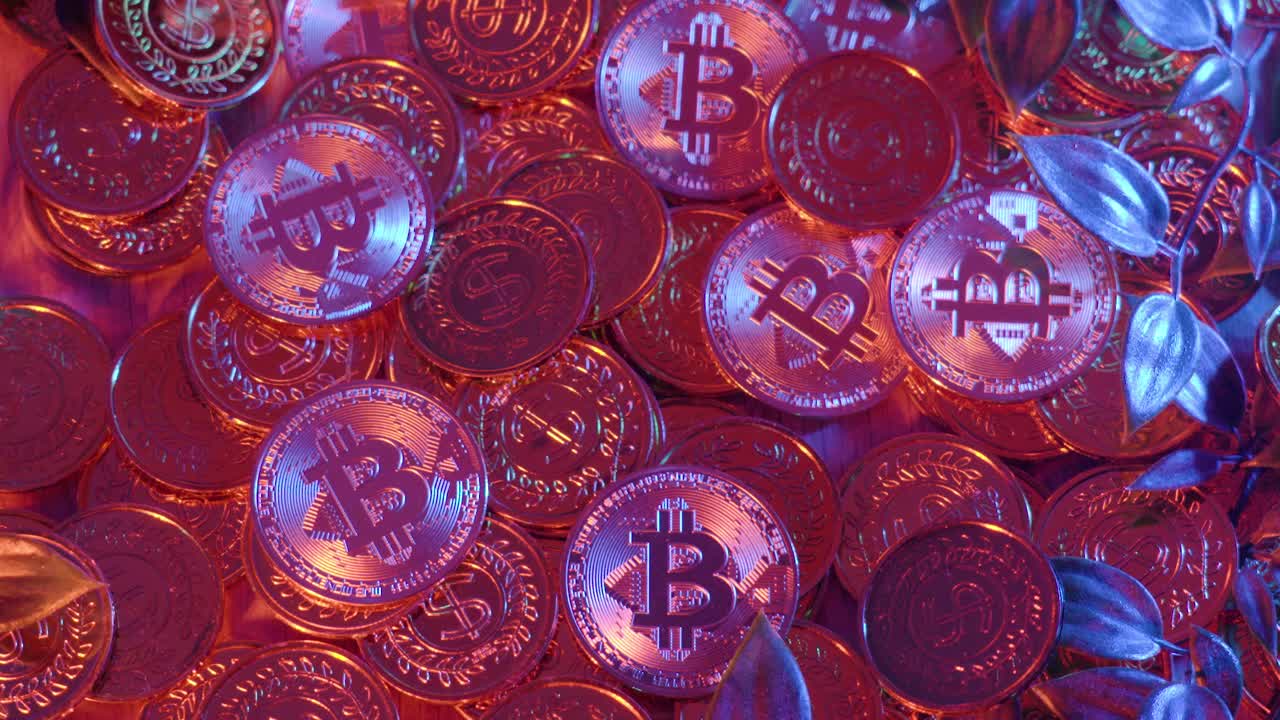 Heap of glowing Bitcoin and cryptocurrency coins bathed in vibrant red light, with blue leaves scattered