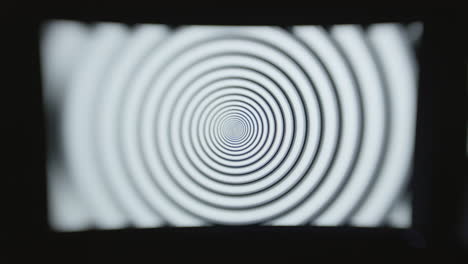 head on shot of a single computer screen with a hypnotic spiral pattern displayed in a dark room with selective focus and a choppy shutter speed effect