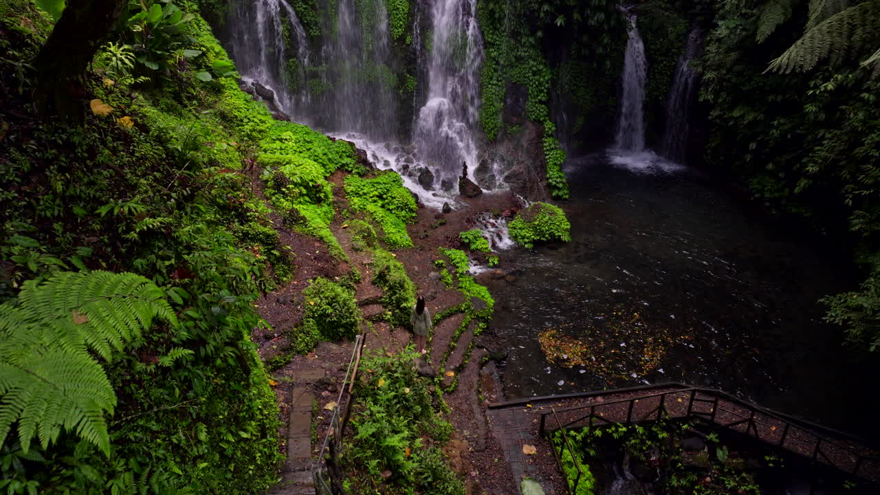 Back view of woman standing and admiring natural pool of Banyu Wana Amertha Waterfall, exotic location in Bali in Indonesia