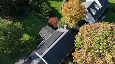 solar panels on roof of house in american neighborhood. colorful trees during sunny autumn day in residential area. aerial circling top down shot.