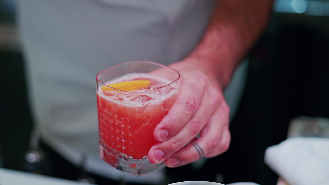 Bartender som plasserer en appelsin i en cocktail i baren