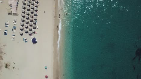 Volando-Sobre-Una-Playa-Organizada-Con-Agua-Azul-Turquesa-Y-Una-Playa-De-Arena-Blanca,-Vista-Superior,-Aérea,-Con-El-Océano-A-La-Derecha