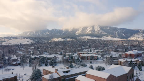 Aerial-drone-moving-backward-over-University-of-Colorado-Boulder-campus-covered-in-snow-on-a-winter-morning-with-the-mountains-of-the-front-range-covered-in-clouds-in-the-background