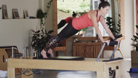 Fit-senior-caucasian-woman-stretching-on-reformer-in-pilates-studio,-unaltered,-in-slow-motion