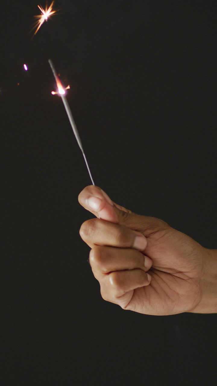 video vertical de la mano de una persona afroamericana sosteniendo una chispa encendida sobre un fondo negro