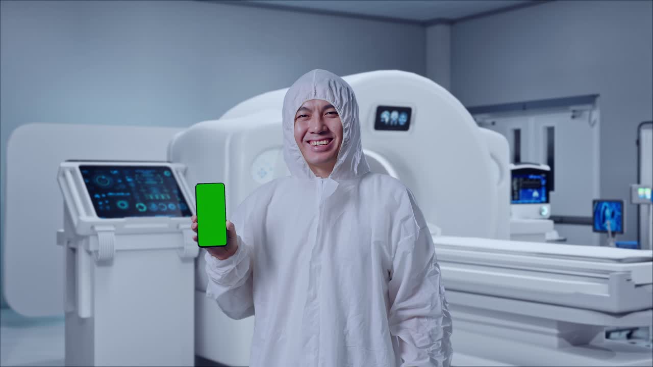 Asian Male Scientist Smiling And Showing Green Screen Smartphone While Standing With MRI Machine In The Hospital