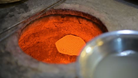 hombre colocando pan tradicional en el horno de tandoor