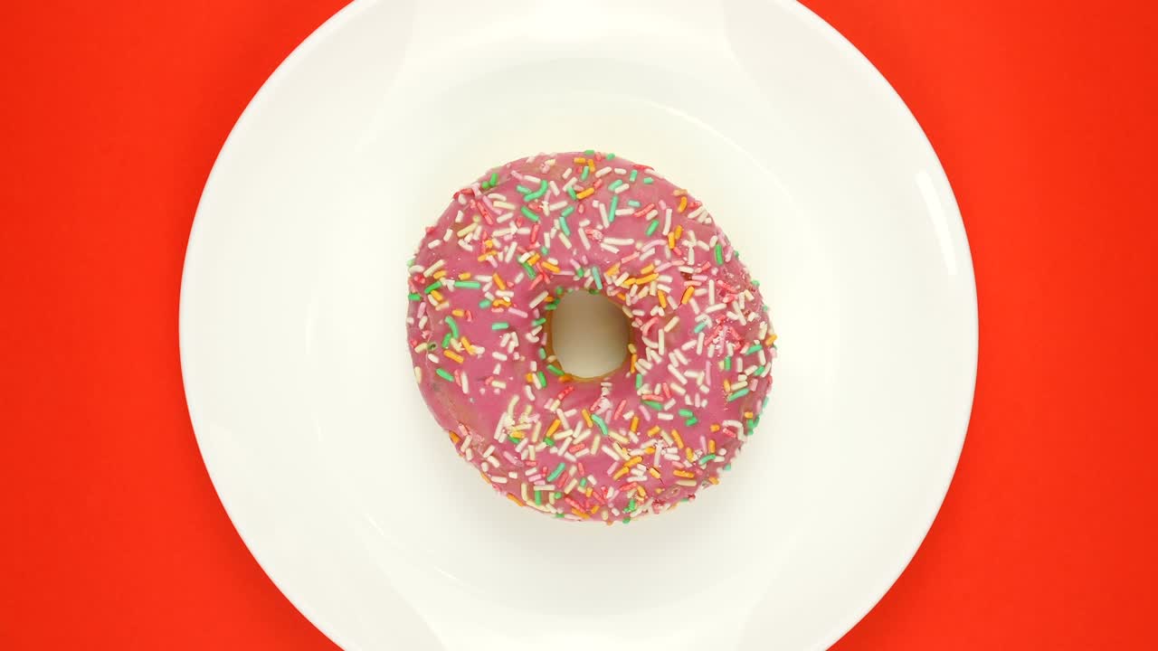 rosquilla recién horneada con esmaltes multicolores girando sobre un fondo rojo.