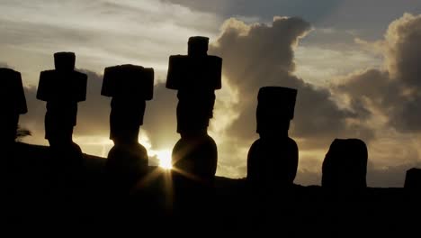 el sol se asoma por detrás de una estatua de la isla de pascua