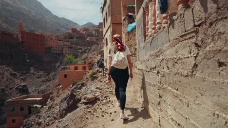 back shot of a young female woman walking through the rugged narrow paths at rural village in the atlas mountains in morocco.