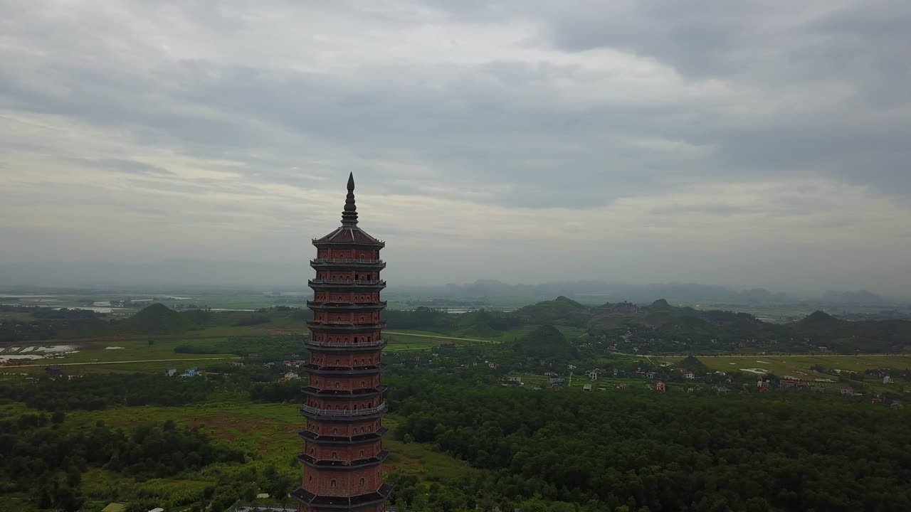 Experience a captivating rotational aerial view of the magnificent Bai Dinh Pagoda in Ninh Binh, Vietnam, showcasing its impressive architecture and the surrounding scenic landscape under a cloudy sky