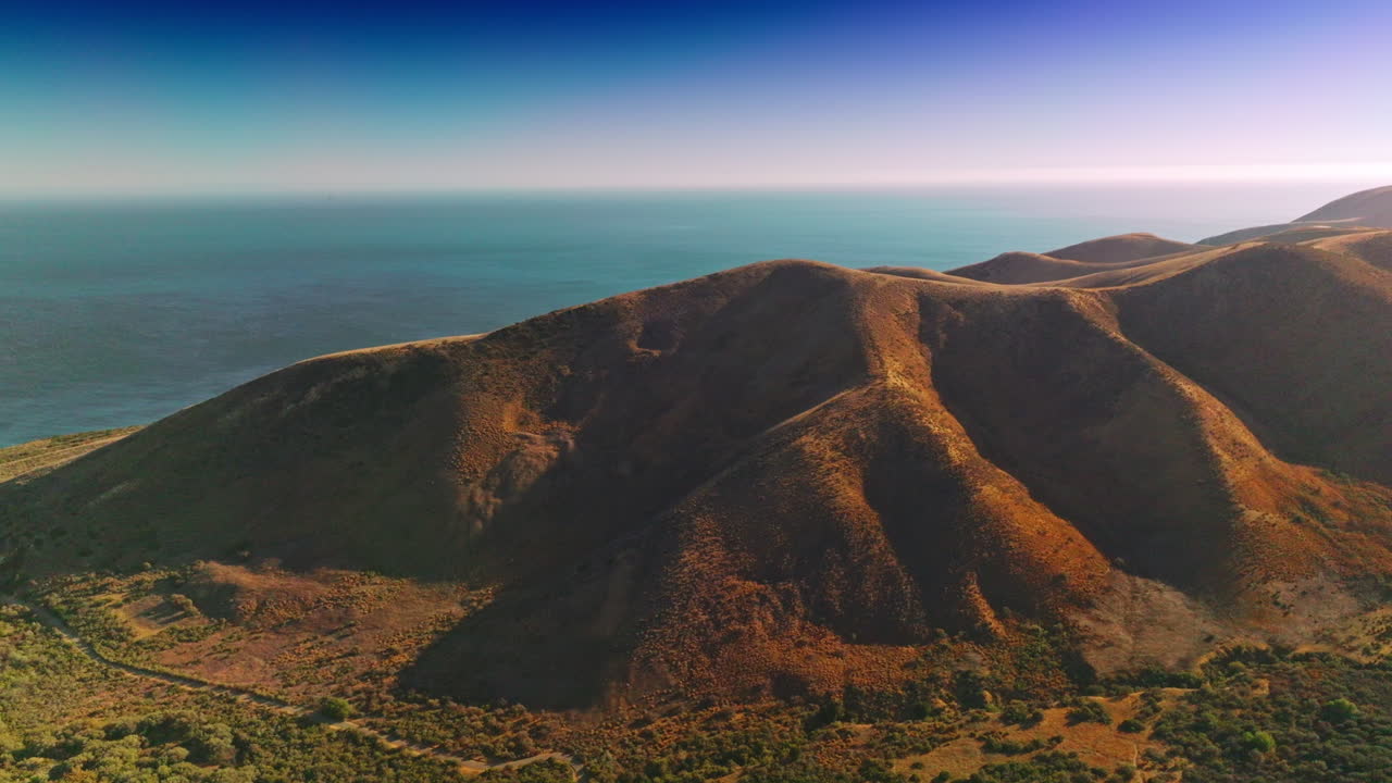 Stunning scenery of mountains locating near the ocean. Drone rising footage over the rocks at the backdrop of blue endless horizon.