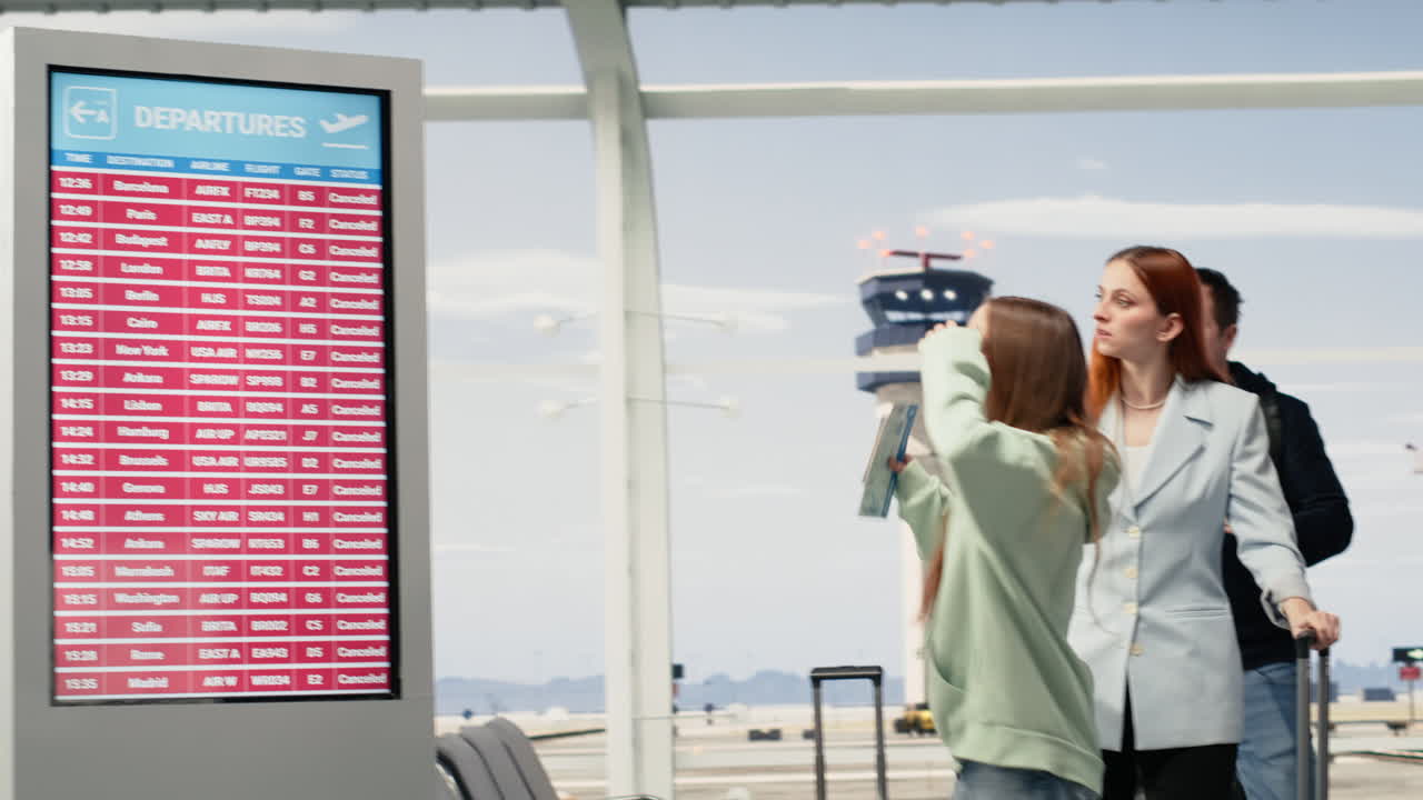 Pasajeros reaccionan a vuelos cancelados y retrasados en la pantalla de salidas del aeropuerto.