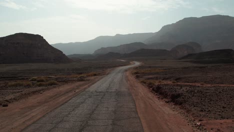 a forward motion drone shot of a parked car near a big road that goes through the desert mountains.