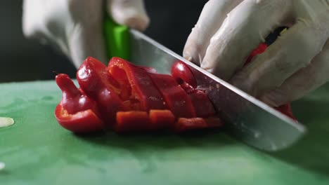 Close-up-man's-hand-slicing-red-fresh-pepper-on-a-cutting-board-with-sharp-knife