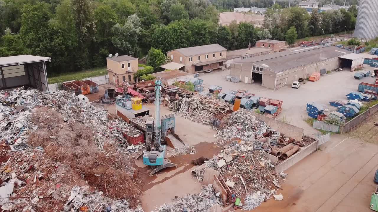 Drone flying over a river in Germany over a metal trash dump site we're a digger is busy with recycling materials