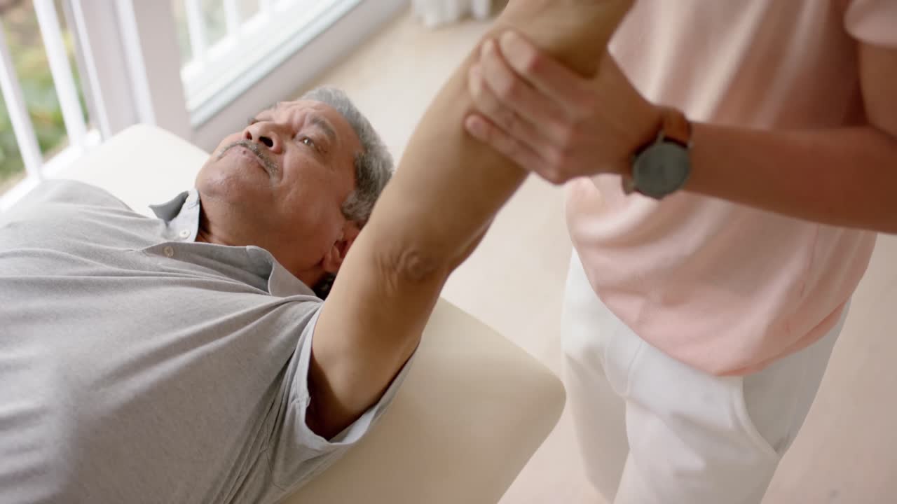 다양한 남성 물리치료사가 조언하고 노인 남성 환자가 소파에서 느린 동작으로 운동합니다.