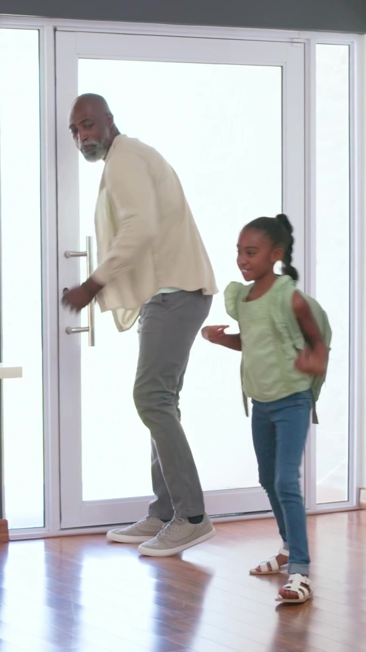 Vertical video: Stepping in girl hugging kneeling man at glass door, greeting, green top, backpack