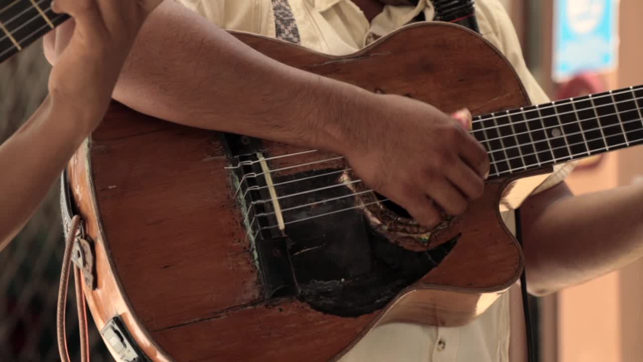 hombre hispano tocando una guitarra vieja, mostrando solo los brazos.