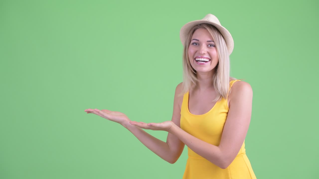 Studio shot of young tourist woman smiling and showing copy space against green background