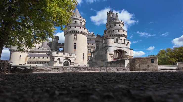 Vista dal basso del Château de Pierrefonds che mostra le due torri rotonde, le mura merlate, gli ingressi ad arco, la pavimentazione in pietra e gli alberi circostanti