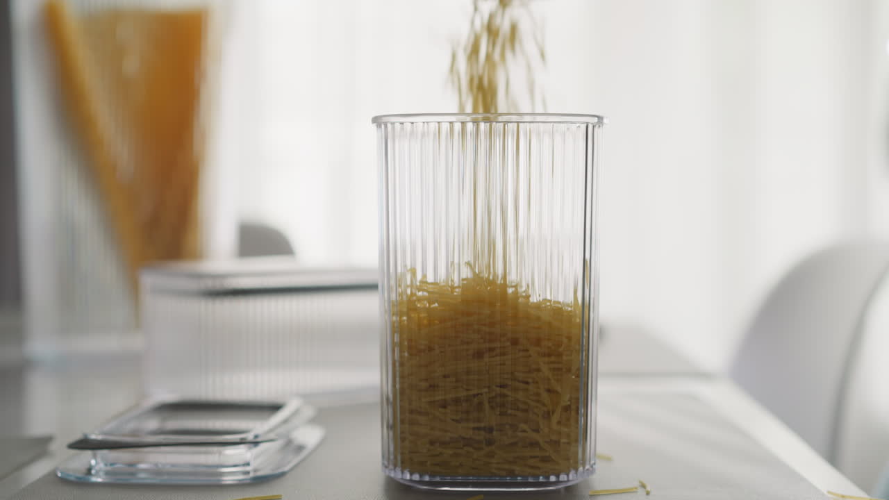 Gli spaghetti cadono in un alto contenitore di plastica sul tavolo della cucina.