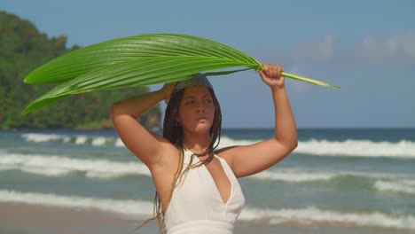 asombrosas sombras femeninas jóvenes bajo una hoja de palma en la playa con olas en el fondo
