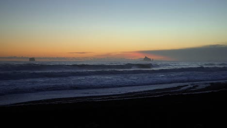 stunning left panning shot of a peaceful sunset at the famous ruby beach in forks, washington with small waves and a small rock formation on a summer evening.
