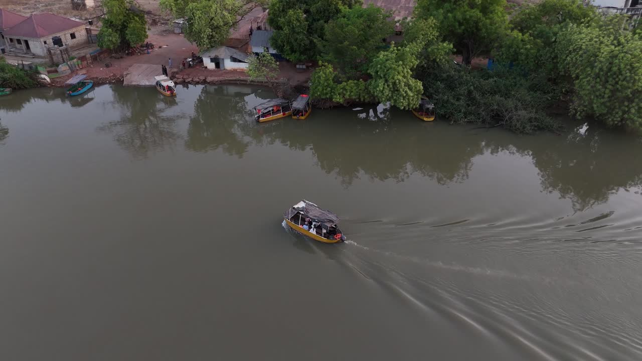Aerial drone view of a wooden boat sailing on the calm waters of the Gambia River at sunset