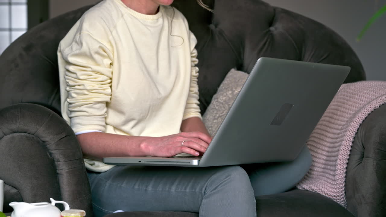 Caucasian woman sitting on a chair and working on her laptop. Table with tea and fruits nearby