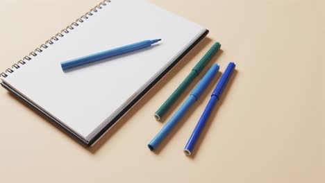 close up of blue markers with notebook on beige background, in slow motion