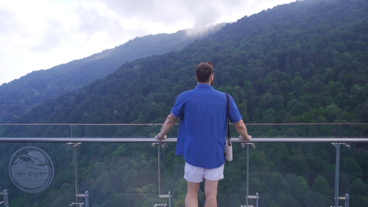 유리 테라스에서 협곡을 바라보는 젊은 남자.