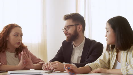 Gruppe-Von-Drei-Multiethnischen-Kollegen,-Die-Am-Tisch-Sitzen-Und-über-Die-Arbeit-Diskutieren-2