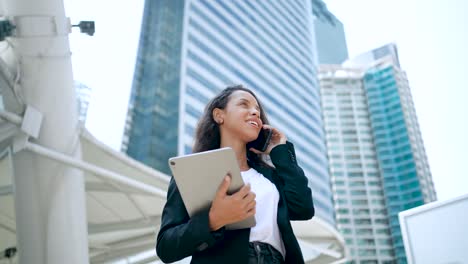 confident and successful hispanic businesswoman with digital tablet standing in the city in financial district, using smartphone walking in the street.