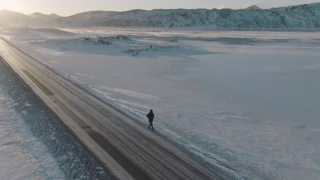 lone hiker on remote highway road in snowy winter iceland landscape, aerial