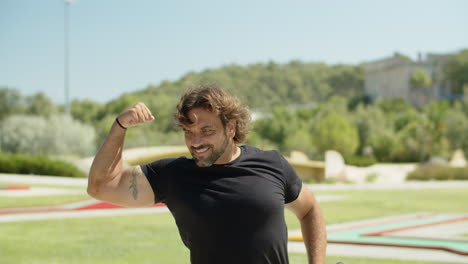 medium shot of happy sportsman showing biceps muscles in park