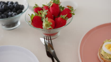 fresh strawberries in glass bowl with blueberries and cutlery on table, at home