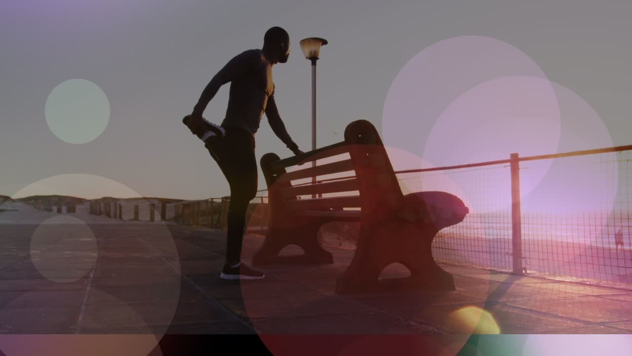 아프리카계 미국인 피트 남자 에 대한 빛 의 반점 들 이 산책로 의 벤치 근처 에 다리를 펴고 있다