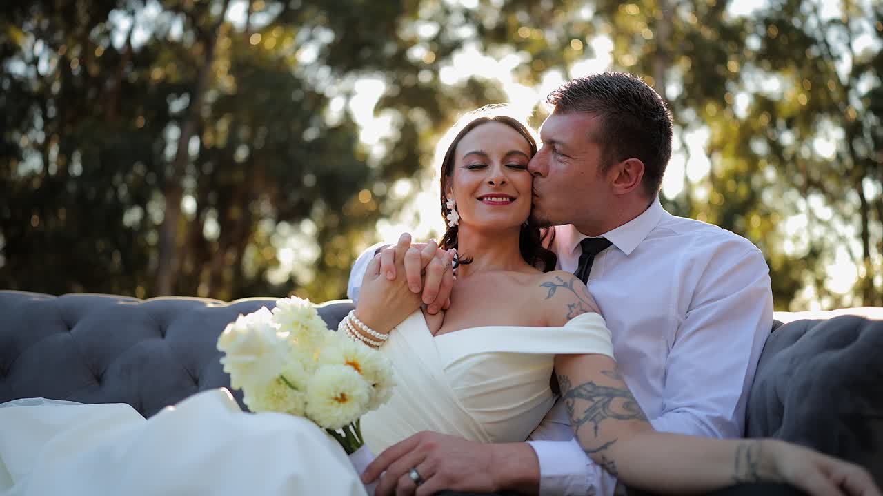 Noivos em contraluz pelo sol do jardim em seu dia de casamento, vistos de um ângulo baixo.
