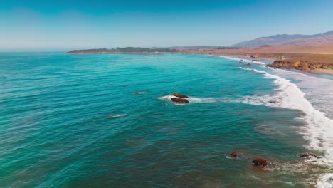 white foamy waves arriving to the shore of morro bay on sunny daytime. lovely calming view of pacific shore from aerial view.