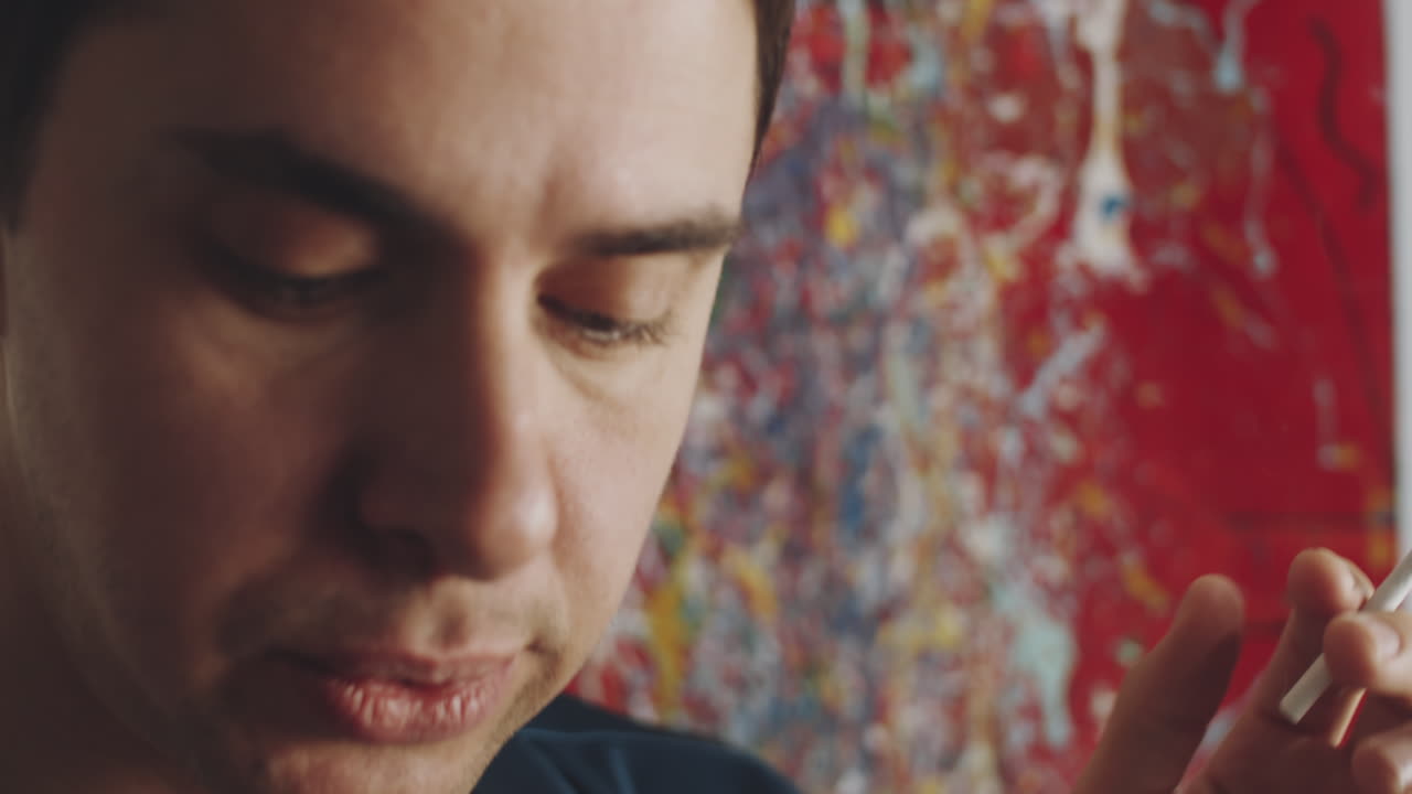 hombre transgénero fumando y hablando por teléfono en casa