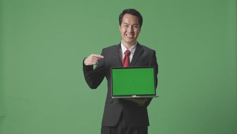 an asian business man showing and pointing to laptop green screen on green screen background in the studio