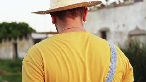 joven granjero bohemio con sombrero y pendientes paseando en cámara lenta a través de la aldea española