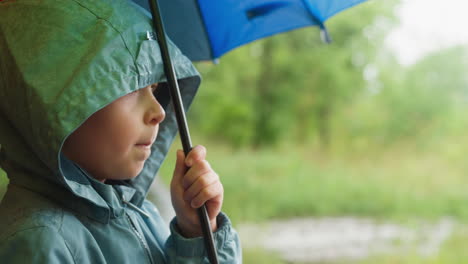 child in hood hides under umbrella from rain thoughtful little boy in waterproof jacket walks with