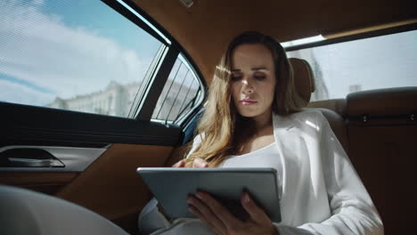 Focused business woman reading data on tablet computer in luxury car.