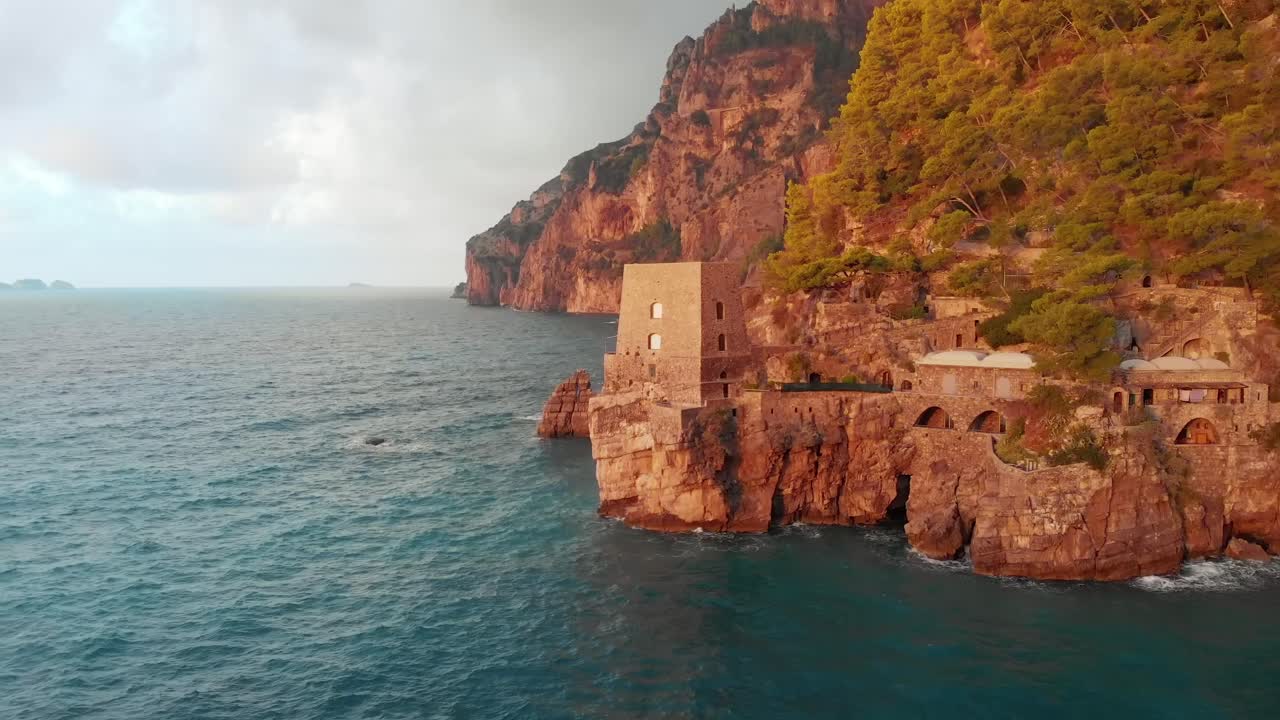 Aerial view of Positano, Italy on a stormy evening. The town is nestled on a cliff overlooking the Mediterranean Sea. The castle, which is rented out as an Airbnb, is perched on the cliff