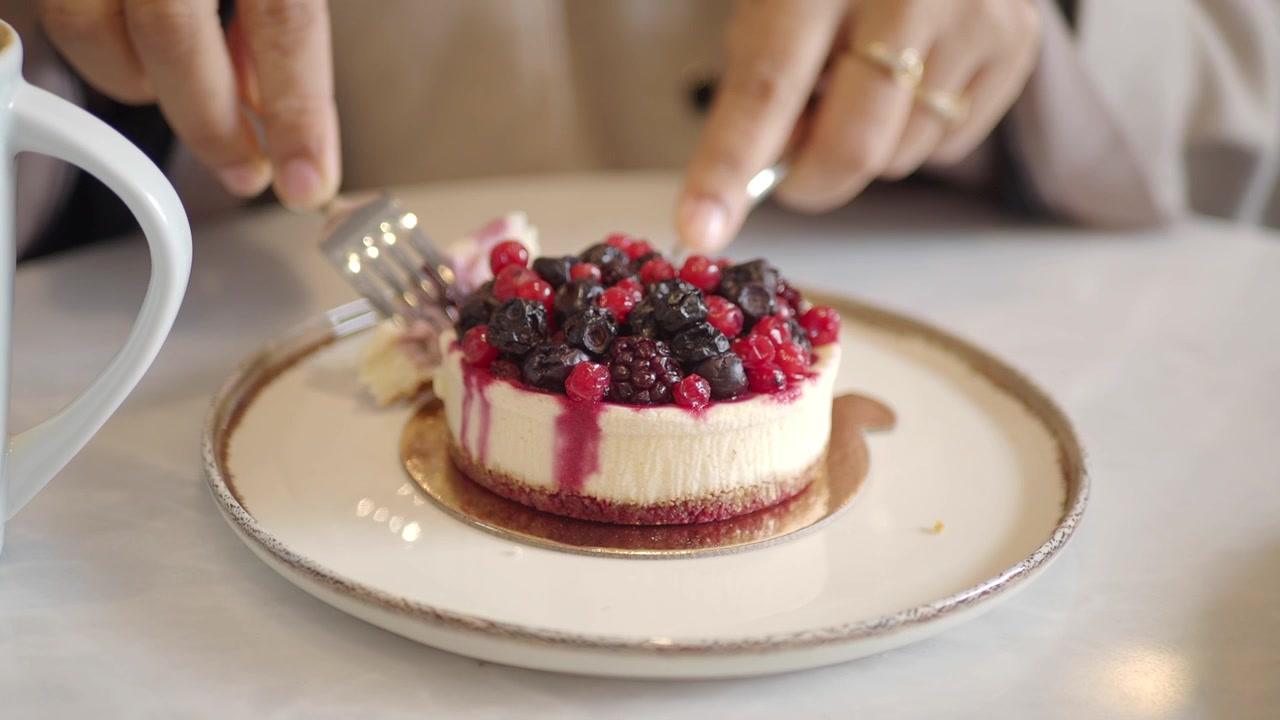 Persona che mangia una deliziosa cheesecake ai frutti di bosco con forchetta e coltello