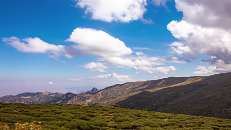 time lapse shot of mountains on sunny arid meadow, moving clouds under blue sky