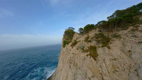 fpv drone volando sobre acantilados rocosos en mallorca y a través de árboles hacia el gran océano